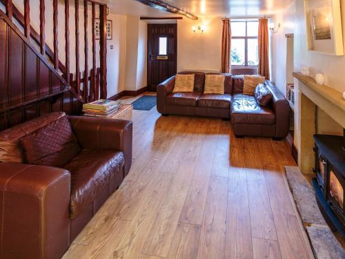 a living room with brown leather furniture and a staircase at Millstone Cottage in Bradwell