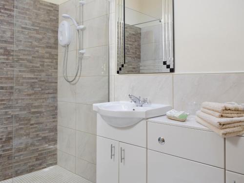 a white bathroom with a sink and a shower at The Coach House At Stable Cottage in Derwydd