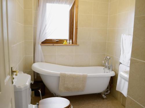 baño con bañera, aseo y ventana en Larachan, en Scarfskerry