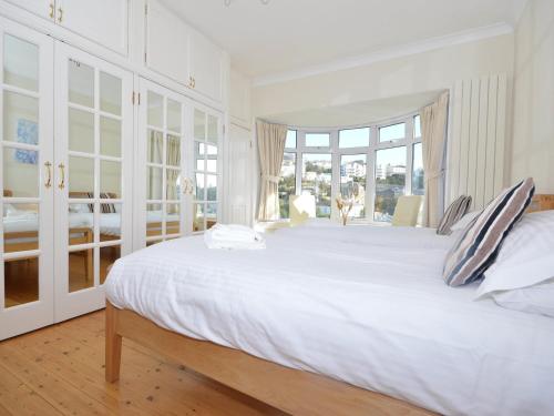 a white bedroom with a large white bed with windows at Rock House in Torquay