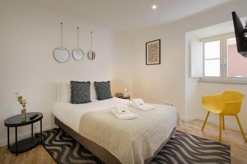 a white bedroom with a bed and a yellow chair at Almoura Ladeira in Évora