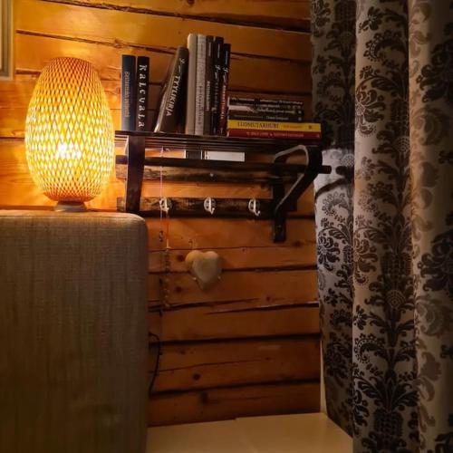 a lamp on a table next to a wall with books at Ainutlaatuinen huoneisto Vanhassa kyläkoulussa in Purola