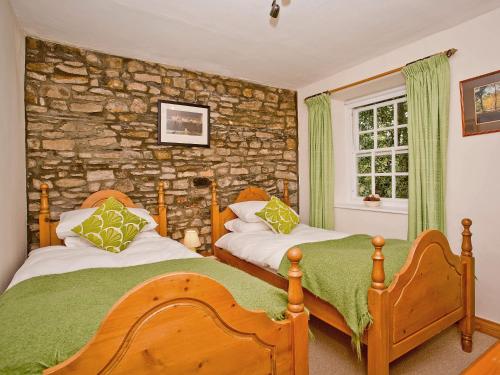 a bedroom with two beds and a stone wall at Cherry Tree Cottage in Bellerby