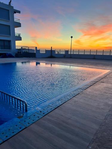 una piscina con puesta de sol en el fondo en The blue pearl-Sensational beach apartment in Aourir en Agadir
