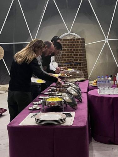 a group of people standing around a table with food at Luxury Desert Camp Oman in Al Wāşil