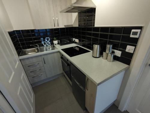 a small kitchen with black tiles on the wall at Queens Holiday Basement in Pembroke Dock