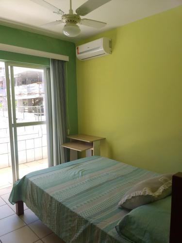 Dormitorio verde con cama y ventana en Condomínio agradável Familiar, en Matinhos