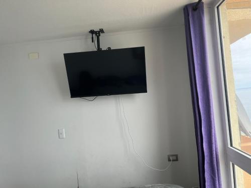 TV de pantalla plana colgada en una pared junto a una ventana en Departamento Playa Bellavista, estacionamiento privado, vista al mar, 2 dormitorios 3 camas en Tomé