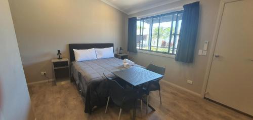 a bedroom with a bed and a table and a window at Sunset Caravan Park Woolgoolga in Woolgoolga