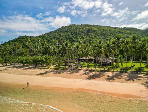a person walking on a beach with palm trees at Eco Sanctuaries Nature Lodge Nacpan Beach, El Nido in El Nido