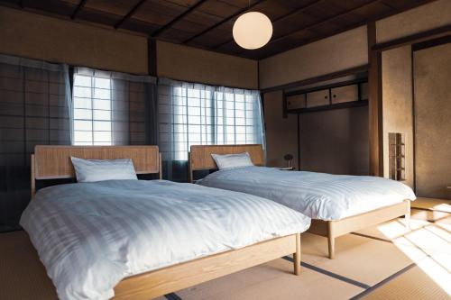 two twin beds in a room with windows at taos 丹波の風土を感じられる一棟貸切の宿 in Sasayama