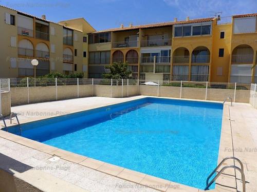 une grande piscine bleue devant un immeuble dans l'établissement Pavillon calme à Narbonne Plage, 6 couchages, grande terrasse, piscine et parking privé - FR-1-229B-67, à Narbonne