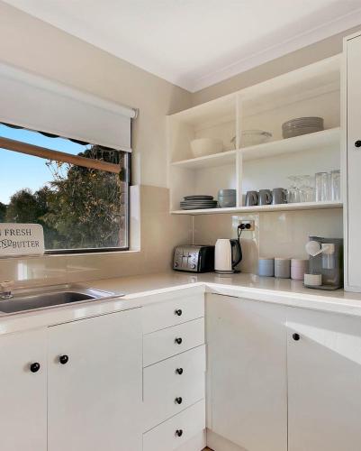 cocina blanca con armarios blancos y ventana en Gundaroo Retreat, en Cromer