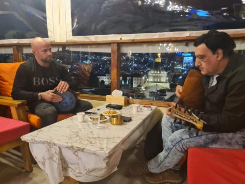deux hommes assis à une table avec une guitare dans l'établissement Seedi Yousef Hostel & Cafe, à Nazareth