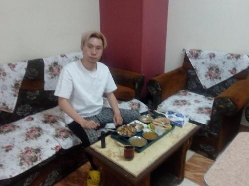 Ein junger Mann, der auf einer Couch mit einem Tisch mit Essen sitzt. in der Unterkunft City Center Guest house and Hostel in Assuan