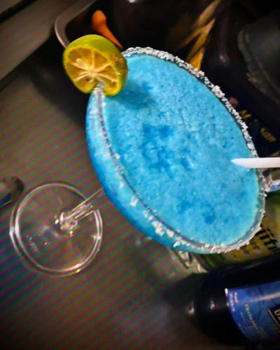 a blue drink with a lime on top of a table at Playa Alegre Beach Resort & Restaurant in Tanauan
