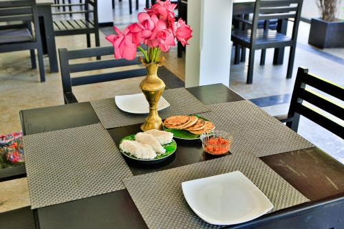 a table with plates of food and a vase with pink flowers at Esprit Bentota in Bentota