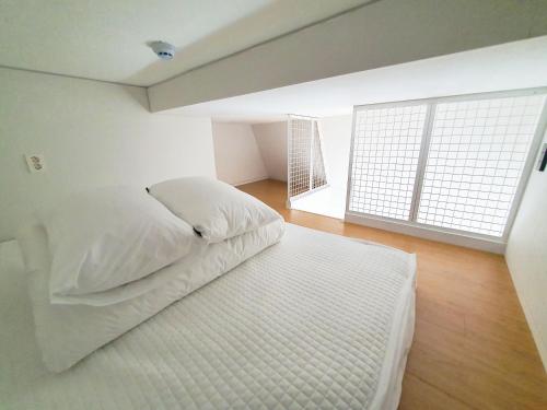 a white bed in a room with a large window at YOLO Guesthouse in Seoul