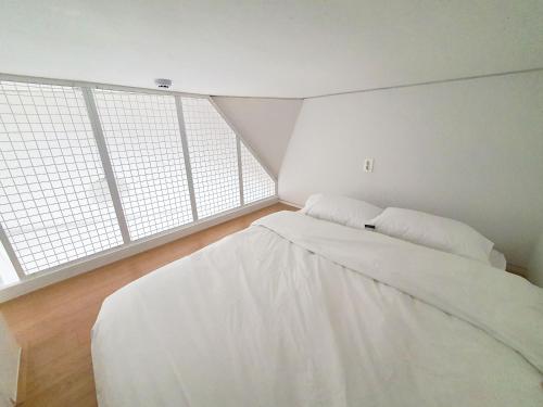 a bedroom with a white bed with two windows at YOLO Guesthouse in Seoul