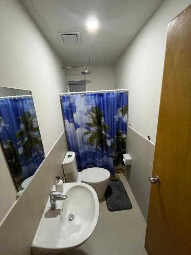 ein Badezimmer mit einem Waschbecken und einem WC mit einem blauen Duschvorhang in der Unterkunft Seafront Residences Vacation Getaway in San Juan