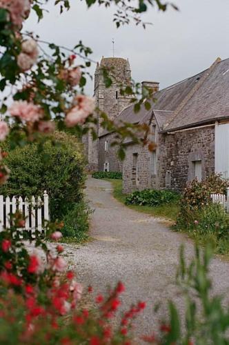 un ancien bâtiment en pierre avec une clôture blanche et des fleurs dans l'établissement Au 3 La Cour à Tôt, à Regnéville-sur-Mer