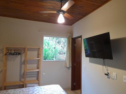 1 dormitorio con ventilador de techo y TV de pantalla plana en Namata CHALÉS en Nova Friburgo