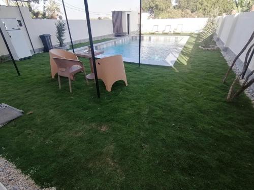 eine Rasenfläche mit zwei Stühlen und einem Tisch sowie ein Schwimmbecken in der Unterkunft Set ma'at in Luxor