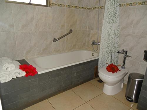 La salle de bains est pourvue de toilettes et d'une baignoire ornée de fleurs rouges. dans l'établissement Hotel Puku Vai, à Hanga Roa