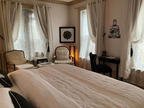 a bedroom with a bed and a desk and windows at Île de Garde B&B in Sherbrooke