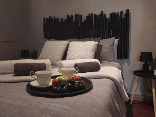 een fruitschaal op een bed met twee kopjes bij Log in @ 118 Self Catering Unit in Meyerton