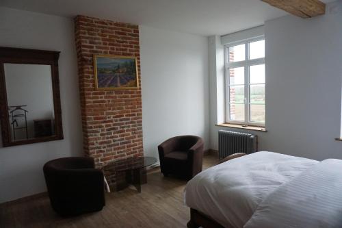 a bedroom with a bed and two chairs and a brick wall at La Ferme Décroué in Saint-Waast-la-Vallée