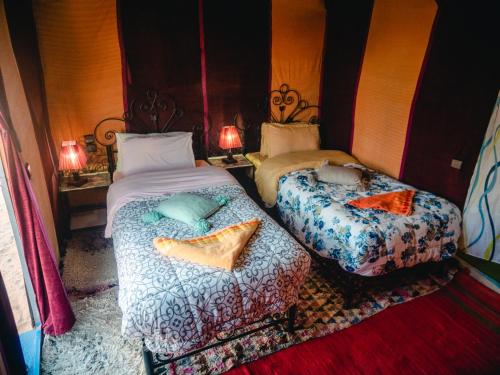 two beds sitting in a room with two lamps at Desert Camp Erg Chebbi in Merzouga