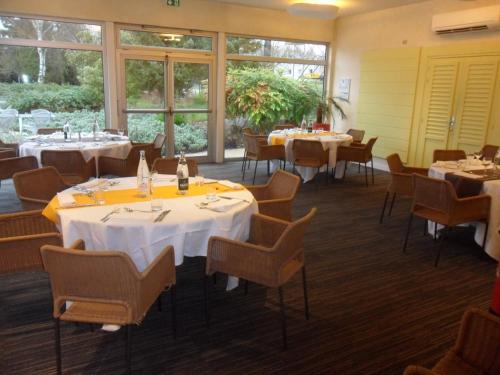 a dining room with tables and chairs and windows at Novotel Amiens Pôle Jules Verne in Boves