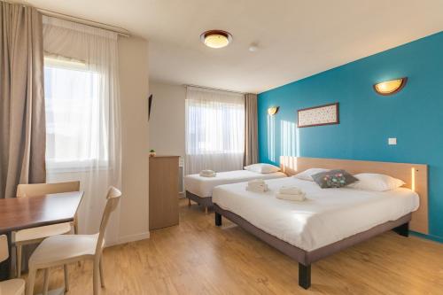 1 Schlafzimmer mit 2 Betten, einem Tisch und einer blauen Wand in der Unterkunft Appart'City Classic La Roche sur Yon Centre in La Roche-sur-Yon