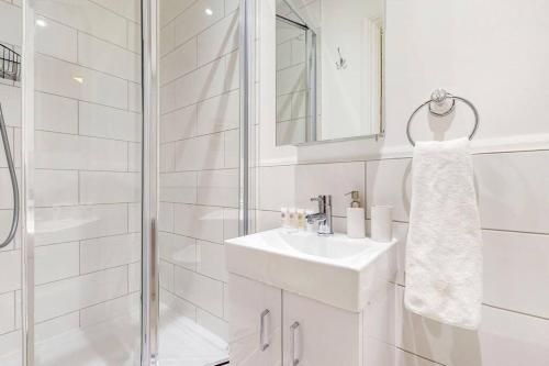 La salle de bains blanche est pourvue d'un lavabo et d'une douche. dans l'établissement Beautiful 4-bedroom house in Victoria Park, à Londres
