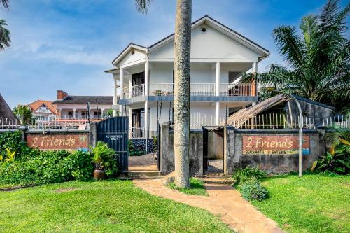 a white house with a gate in front of a yard at 2 Friends Beach Hotel in Entebbe