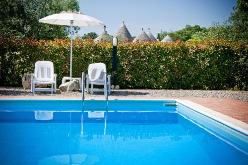 zwei Stühle und ein Sonnenschirm neben einem Pool in der Unterkunft Trulli Il Castagno in Martina Franca