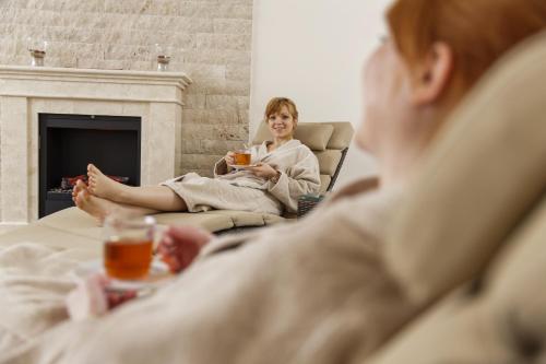 a woman in a robe sitting in a room with a fireplace at Hotel Saigerhöh Wellness Spa Golf Wandern über dem Titisee in Lenzkirch
