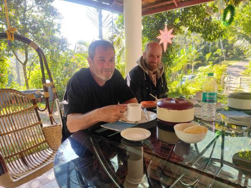 two men sitting at a table with a cup of coffee at Thoppil Homestay Munnar in Munnar