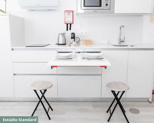 a kitchen with white cabinets and two stools at TRIADE Apartamentos in Aveiro