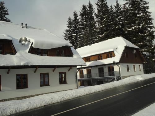 two houses covered in snow next to a road at Penzion Dominik in Železná Ruda