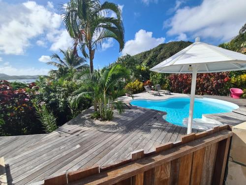 a swimming pool with an umbrella and a wooden deck at La Villa Baie du Marin in Le Marin