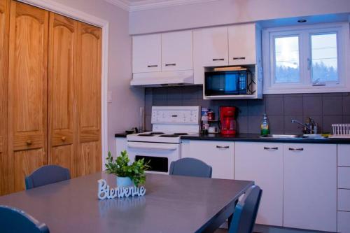 a kitchen with white cabinets and a table and a microwave at Chalet Le Marin à 5 minutes du centre ville in Sainte-Flavie