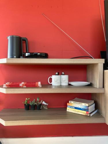 una pared roja con estanterías de madera con tazas y libros en Apartamentob301 coliving bombinhas, en Bombinhas