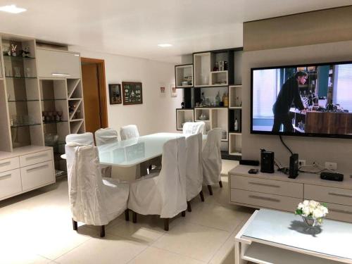sala de estar con mesa, sillas blancas y TV en Paraíso do Atlântico Club Residence, en Cabedelo