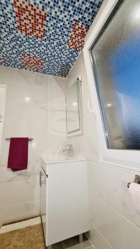 a white bathroom with a sink and a window at Appartement très lumineux in Sevran