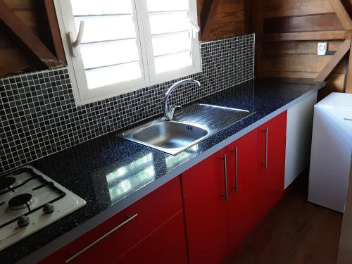 cocina con armarios rojos, fregadero y ventana en Gite de Paulo la source en Pointe-Noire