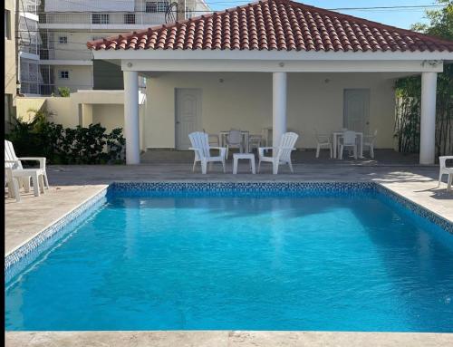 a pool with chairs and a table and a house at Beautiful Condo in La Romana with pool near Caleta Beach in La Romana