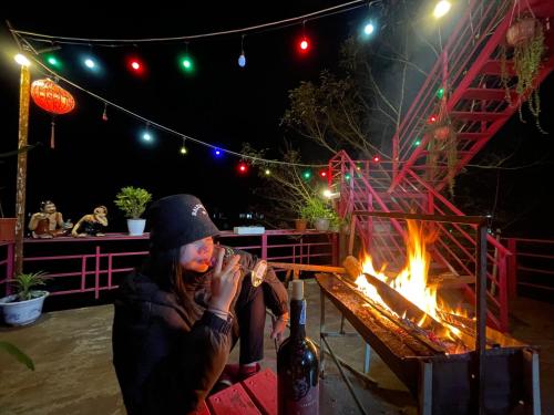 Eine Frau, die am Feuer mit einer Flasche Wein sitzt. in der Unterkunft Cornflower Homestay PHONG NHA in Phong Nha