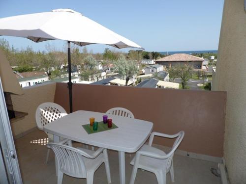 une table et des chaises blanches sur un balcon avec un parasol dans l'établissement Appartement studio cabine mezzanine, 4-6 couchages, parking privé, proche plage - FR-1-326-592, à Marseillan